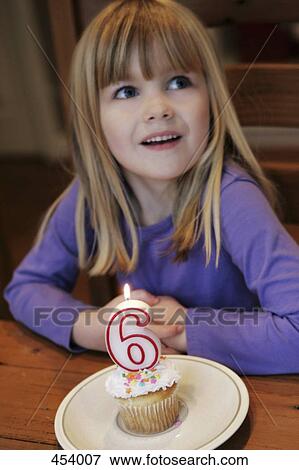 Stock Photo - Young girl sitting at a table with a lit candle on a cupcake. Fotosearch