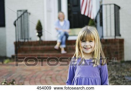 Young girl standing on a pathway in front of a house with her mother sitting behind on the doorstep View Large Photo Image Stock Photo - Young girl standing on a pathway in front of a house with her mother sitting behind on the doorstep. Fotosearch