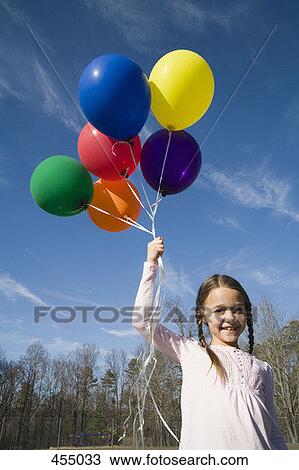 Stock Image - Young girl holding helium balloons. Fotosearch