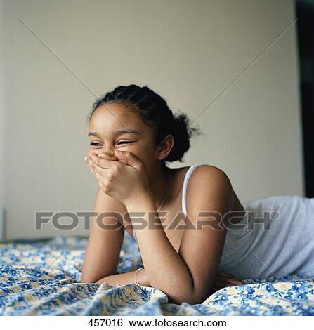 Stock Photograph - Girl lying on her bed laughing. Fotosearch