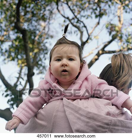Stock Image - Mother carrying baby girl over her shoulder. Fotosearch