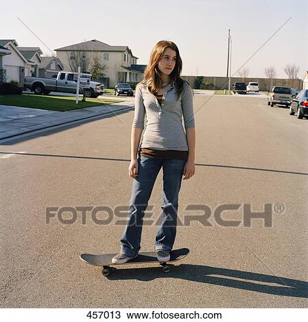 Stock Image - Teenage girl standing on skateboard in the street. Fotosearch