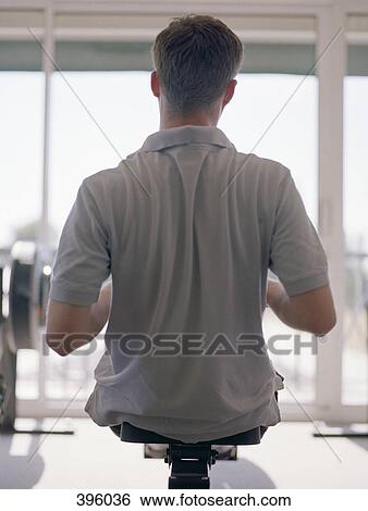 Stock Photograph - Rear view of man using rowing machine. Fotosearch