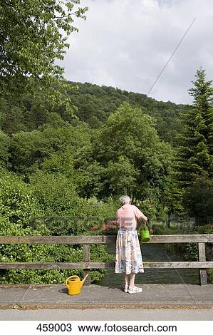 Stock Image - A senior woman watering flowers in a flower box. Fotosearch