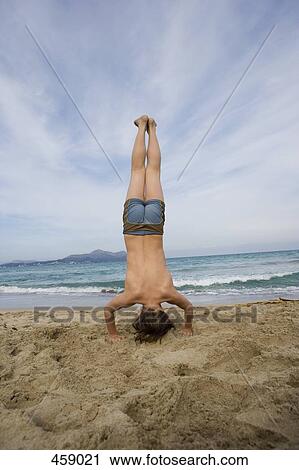 Stock Image - Rear view of a boy doing a headstand on a beach. Fotosearch