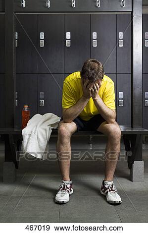 Stock Photo - A man sitting with his head in his hands in a locker room. Fotosearch