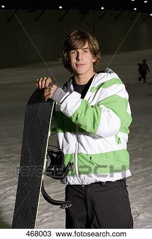 Stock Image - Young man standing on a ski slope with a snowboard. Fotosearch