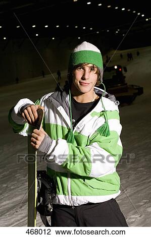 Young man standing on a ski slope with a snowboard View Large Photo Image Stock Image - Young man standing on a ski slope with a snowboard. Fotosearch