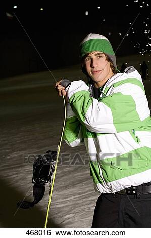 Young man standing on a ski slope with a snowboard View Large Photo Image Stock Photograph - Young man standing on a ski slope with a snowboard. Fotosearch