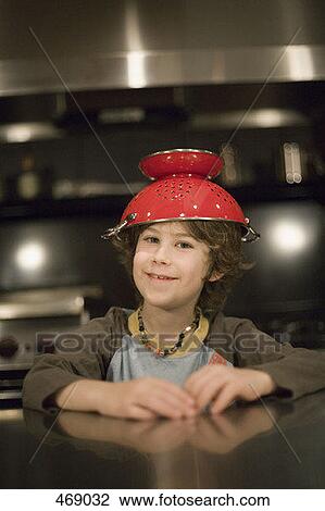 Stock Image - Young boy in a kitchen counter with a colander on his head. Fotosearch
