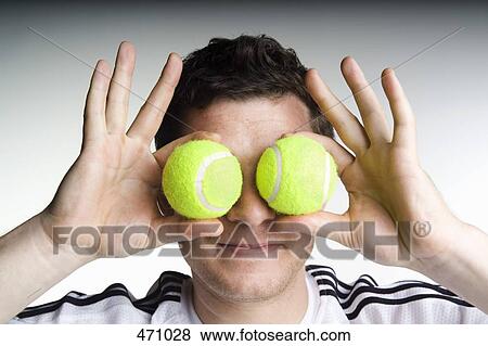 A man holding two tennis balls in front of his face View Large Photo Image Stock Photo - A man holding two tennis balls in front of his face. Fotosearch