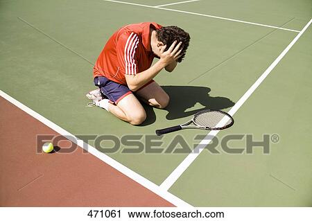 Stock Image - A tennis player kneeling on the court in defeat. Fotosearch