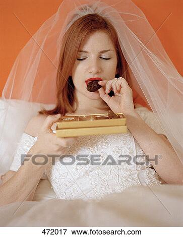 A bride sitting on a bed eating a box of chocolates View Large Photo Image Stock Photo - A bride sitting on a bed eating a box of chocolates. Fotosearch