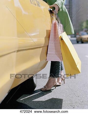 A woman holding shopping bags and opening a taxi door, New York City, USA View Large Photo Image Picture - A woman holding shopping bags and opening a taxi door, New York City, USA. Fotosearch