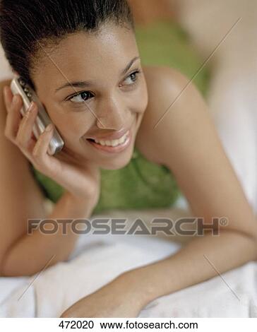 A woman lying on a bed using a mobile phone View Large Photo Image Stock Image - A woman lying on a bed using a mobile phone. Fotosearch