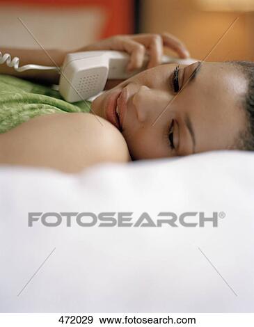A woman lying on a bed using a telephone View Large Photo Image Stock Photo - A woman lying on a bed using a telephone. Fotosearch