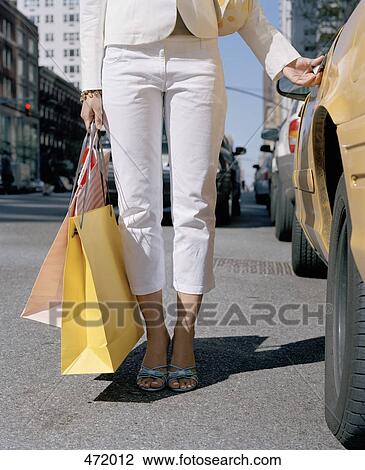 Stock Image - Woman holding shopping bags by a taxi. Fotosearch