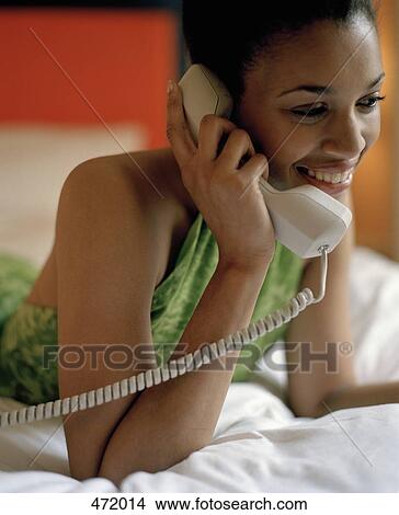 Woman lying on a bed using a telephone View Large Photo Image Picture - Woman lying on a bed using a telephone. Fotosearch
