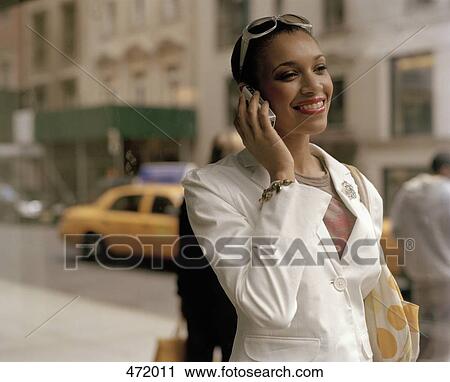 Stock Image - Woman using a mobile phone whilst standing on the sidewalk. Fotosearch