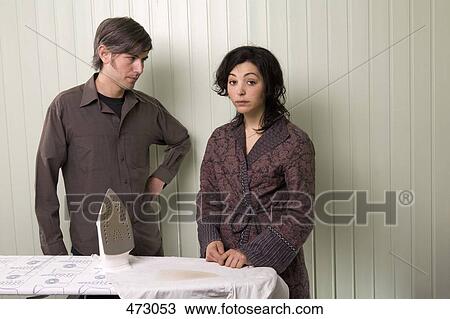 Stock Image - A man and a woman standing next to a burnt shirt on an ironing board. Fotosearch