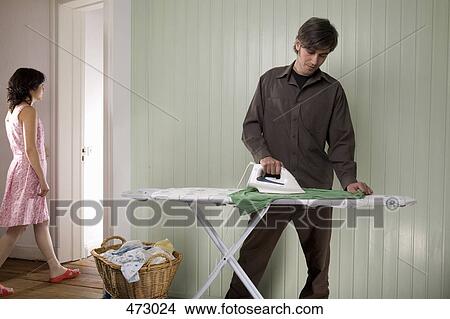 Picture - A man ironing whilst a woman is walking into another room. Fotosearch