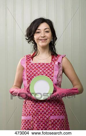 A woman holding a plate whilst wearing an apron and rubber gloves View Large Photo Image Picture - A woman holding a plate whilst wearing an apron and rubber gloves. Fotosearch