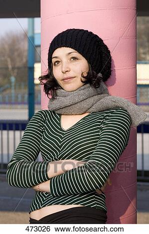 Stock Photograph - A woman leaning against a column and wearing a scarf and hat. Fotosearch