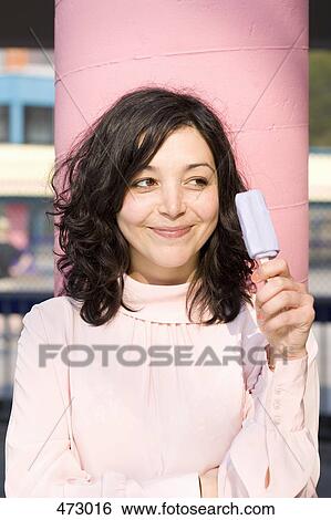 Stock Photograph - A young woman holding an ice-cream on a stick. Fotosearch