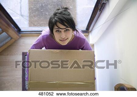 Stock Image - Teenage girl carrying box through doorway. Fotosearch
