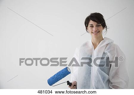 Picture - Teenage girl holding a paint roller and wearing overalls. Fotosearch