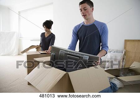 Stock Image - Two teenagers unpacking boxes. Fotosearch