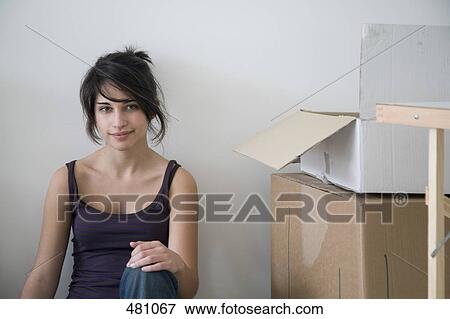Stock Photo - Young woman sitting next to cardboard boxes. Fotosearch