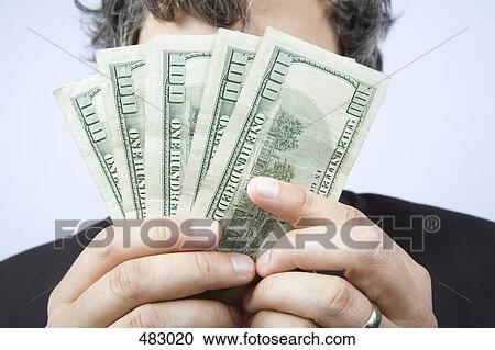 A businessman holding a fan of hundred dollar bills in front of his face View Large Photo Image Stock Image - A businessman holding a fan of hundred dollar bills in front of his face. Fotosearch
