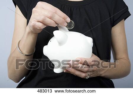 Detail of a woman holding a coin above a piggy bank View Large Photo Image Stock Image - Detail of a woman holding a coin above a piggy bank. Fotosearch