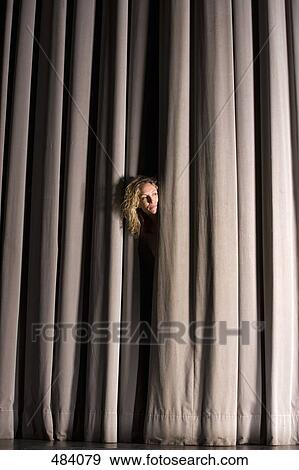 Stock Photo - A woman peeking through a stage curtain. Fotosearch