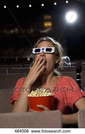 A woman sitting in a movie theater wearing 3-D glasses and eating popcorn View Large Photo Image Stock Photo - A woman sitting in a movie theater wearing 3-D glasses and eating popcorn. Fotosearch