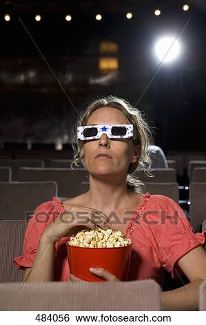 A woman sitting in a movie theater wearing 3-D glasses and eating popcorn View Large Photo Image Stock Photograph - A woman sitting in a movie theater wearing 3-D glasses and eating popcorn. Fotosearch