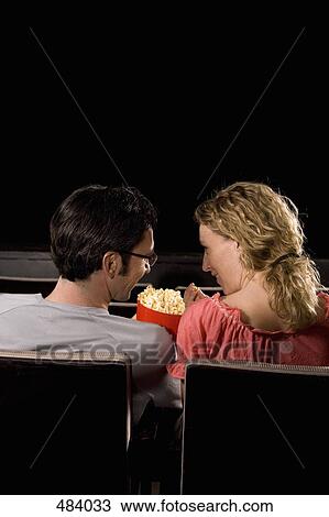 Stock Image - Rear view of a mid adult couple sitting in a movie theater. Fotosearch