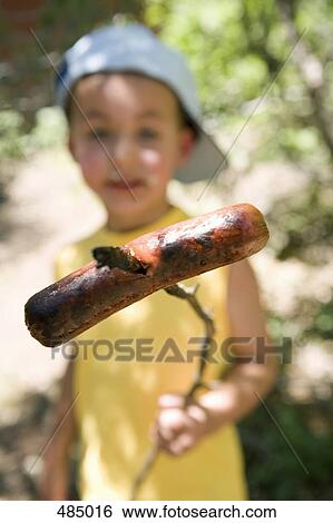 A young boy holding a cooked sausage on a stick View Large Photo Image Stock Photograph - A young boy holding a cooked sausage on a stick. Fotosearch