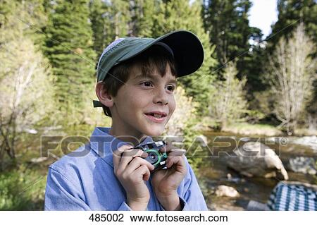 Stock Image - A young boy holding a disposable camera by a river. Fotosearch