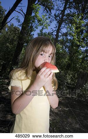 Stock Photo - A young girl eating a piece of watermelon in a forest. Fotosearch