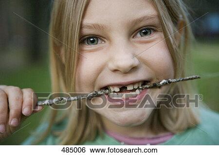 Stock Photograph - A young girl with a missing front tooth biting a stick. Fotosearch