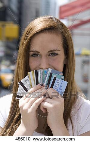 Stock Image - An adolescent girl holding a fan of credit cards over her mouth. Fotosearch