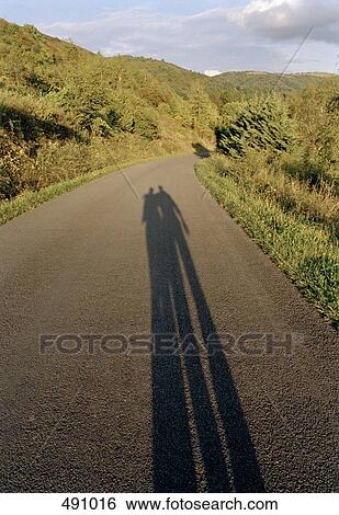 Shadows of two people standing on a country road View Large Photo Image Stock Photograph - Shadows of two people standing on a country road. Fotosearch