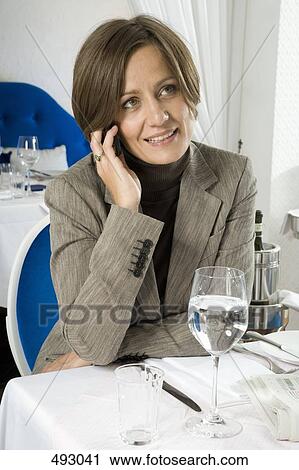 Stock Image - A businesswoman on her mobile phone in a restaurant. Fotosearch