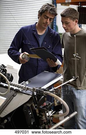 Stock Image - A man training a young man in a printing factory. Fotosearch