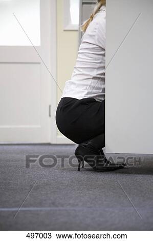Stock Image - A woman crouching in front of an open cupboard. Fotosearch