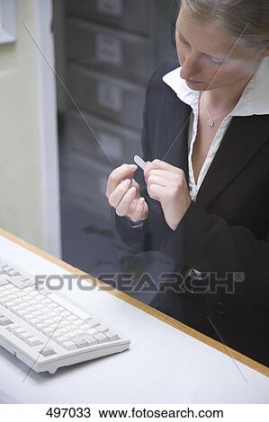 Stock Image - A woman sitting at a desk and filing her nails. Fotosearch