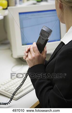 A woman sitting at a desk and holding a telephone receiver View Large Photo Image Stock Image - A woman sitting at a desk and holding a telephone receiver. Fotosearch