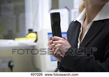 A woman sitting at a desk and holding a telephone receiver View Large Photo Image Stock Photograph - A woman sitting at a desk and holding a telephone receiver. Fotosearch